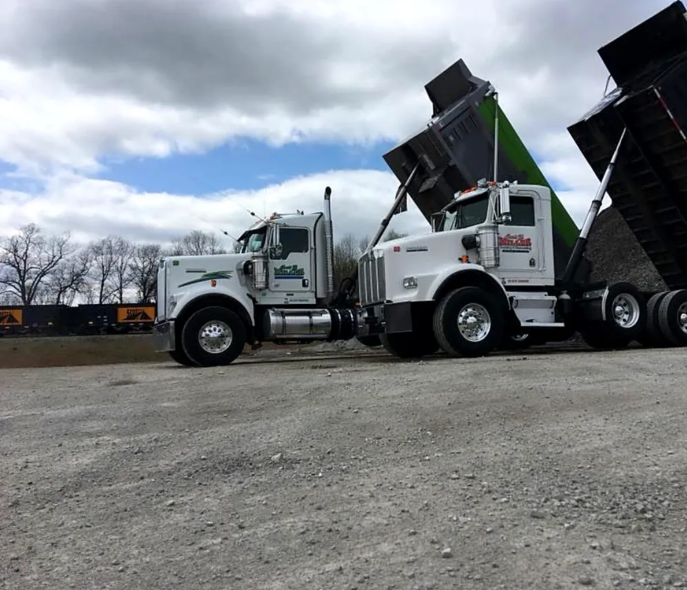 Tri-axle dump trucks unloading on a site